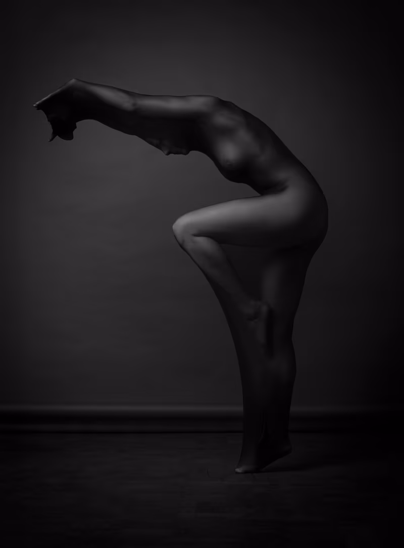 Silhouetted figure in a forward bend pose against a dark gray background with dramatic lighting emphasizing body contours.